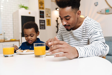 Fototapeta na wymiar Pleased african american father and son having breakfast at home