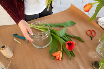 Woman florist working on creating a creative bouquet of tulips for a client. Top view. Fresh white and red tulips in flower shop. Florist's desk with scissors, vases and secateurs.