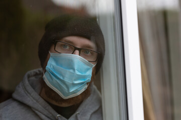 Fototapeta na wymiar Young male looking out of window with face mask on. Lock down. Quarantine