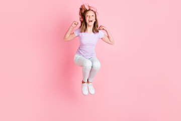 Full length photo of cheerful happy small girl raise fists jump up win isolated on pink color...