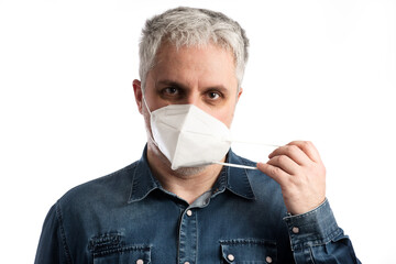 Middle age man in blue jeans shirt puts on a face mask - isolated on white background with clipping path included. White epidemic mask for protection against viruses and bacteria