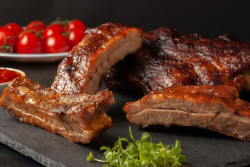 Grilled pork ribs, served on a graphite board with tomatoes