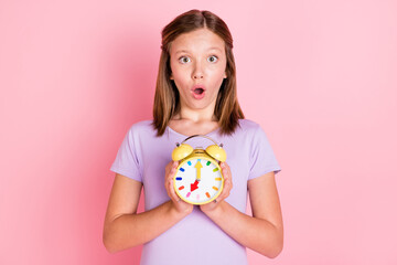Photo of shocked amazed little teenage girl hold hands alarm clock time isolated on pink color background