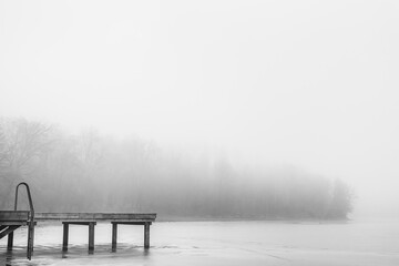 A wooden pier with the view on a foggy frozen lake