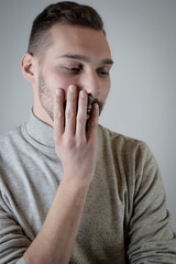 Portrait of a young man with a short beard with his hand on his cheek with thoughtful gaze 