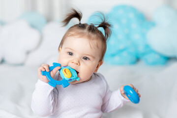 baby bites a rodent or toy with his teeth on the bed at home, teething