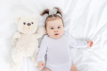 baby with a teddy bear lying on the bed at home, the concept of play and development of children