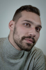 Fototapeta premium Portrait of a young brown-haired man with a short beard and a gray turtleneck sweater 