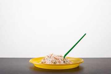 salad in a plastic disposable plate with a stuck fork on a white background