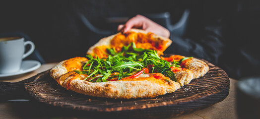 woman Hand takes a slice of Pepperoni Pizza with Mozzarella cheese, salami, Tomatoes, pepper, Spices and Fresh arugula in cafe