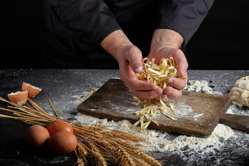 Homemade raw noodles made from flour, egg on wooden bowl on black. Chef hands