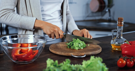 Cropped view of woman cutting lettuce near bowl and vegetables on blurred foreground