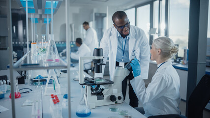 Modern Medical Research Laboratory: Two Scientists Working Together Using Microscope, Analysing...