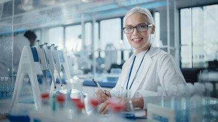 Medical Research Laboratory: Portrait of a Beautiful Female Scientist Writing Down Data, Smiling on Camera. Advanced Scientific Lab for Medicine, Biotechnology, Microbiology Development