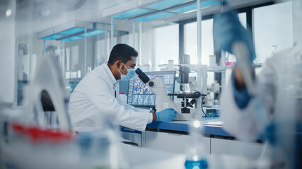 Medical Research Laboratory: Male Scientist Looking Under Micrsocope, Analyzing Samples. Advanced...