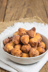 Homemade Castagnole, Mutzen or Castagnole, typical german or italian carnival fritters with sugar in a white bowl on rustic wooden table, vertical with copy space.