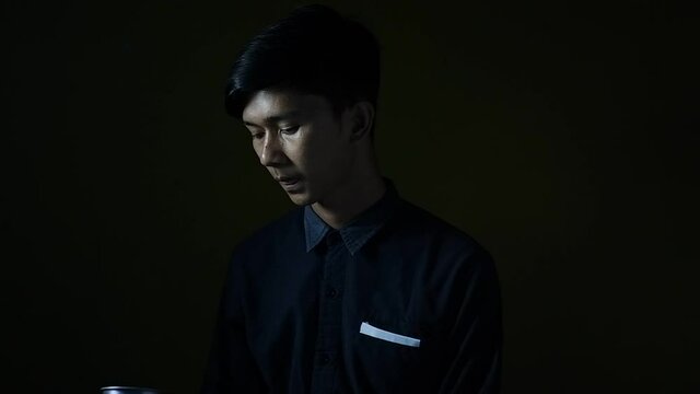 portrait of an asian man drinking coffee in a dark room. the concept of relaxing in the solitude of the night. aloof person with isolated black background