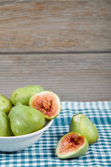 Green figs in a white bowl and on a wooden table with blue tablecloth