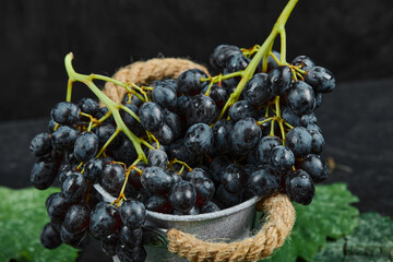 A bucket of black grapes with leaves on black background, close up