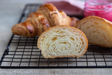 Fresh crispy croissants with pink honey on black metal grille, concrete background.
