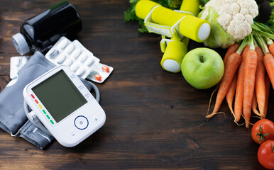 Blood pressure monitor, pills, dumbbells and fresh fruits with vegetables against wooden table. Healthy lifestyle and prevention of hypertension concept
