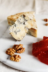 Slice of blue aged Stilton cheese accompanied with quince marmalade or jelly or jam Spanish dulce de Membrillo and walnuts on white marble tray. Selective focus