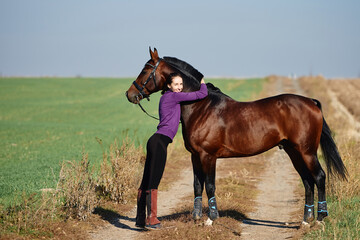 Young female farmer taking care about horse on ranch on summer day, copy space. Girl stroking and...