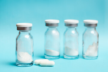 Glass vials with medicine in powder form and two white capsules on a blue background, soft focus