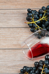 Top view of a bunch of black grapes and a glass of wine on wooden background