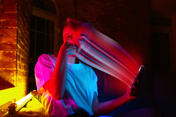 Cinematic portrait of stylish woman in neon lighted interior using a smartphone. The face is...