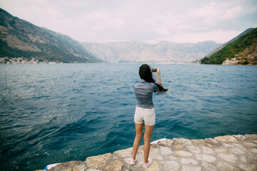 Fototapeta na wymiar A woman stands on the pier and takes pictures of the Bay of Kotor 
