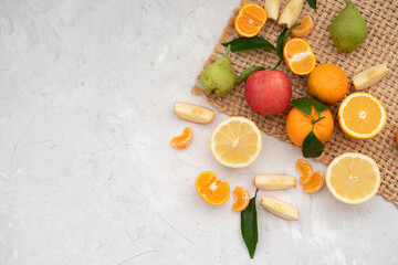 Many different fruits: tangerines, oranges, grapefruits, apples and pears on pale grey table with brown napkin. Fruits contain many vitamins, prepare fresh juices useful for healthy lifestyle.