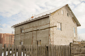 Fototapeta na wymiar concrete house behind a wooden fence. snow covered earth. construction of a residential building in the background. scaffolding at a construction site. Construction in various forms