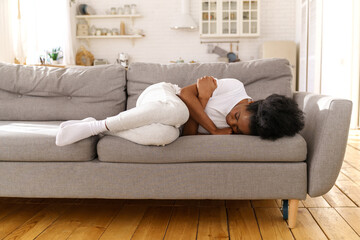 Unhappy depressed African American woman lying on couch, sleeping, feeling unwell and unhealthy. Frustrated upset Black girl with arms crossed crying, suffering from divorce or break up. Mental health