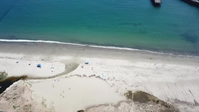 Aerial flyover of clean sandy beach with blue turquoise ocean and a flock of seagulls flying over the water