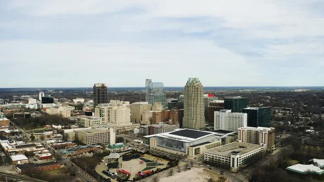 Giant screen on the outside of a shopping center in downtown Raleigh with the high buildings in the skyline in the background on a partly cloudy day. Drone shot dolly high altitude shot