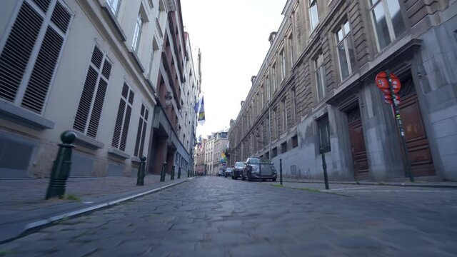 Low Forward Dolly shot over historic cobblestone road in city center of Brussels, Belgium, with streets parked in the car, Brussels flag hanging down the street.