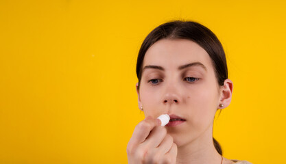 Attractive young woman using hygienic lipstick on yellow background. lips care and protection. woman applying balm on lips