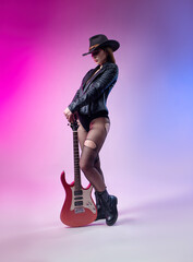 Fototapeta na wymiar fashionable stylish woman in black leather jacket and hat with guitar on neon background