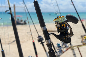 Foreground fishing rod and reel facing the sea, in the background the Caribbean Ocean and boats moored in a Mexican beach