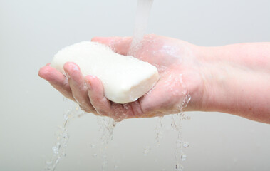 A bar of soap in a woman's hand. A stream of water from the tap pours on the hand. Concept-hygiene, quarantine