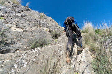 Unrecognized young boy wearing sportswear climbing the mountain during sunny day.