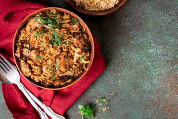 Spicy bulgur with mushrooms, onions, dill, and cumin in a bowl on a dark background top view. Bulgur stewed with mushrooms. Arabic cuisine, vegan and vegetarian food. Copy space for text