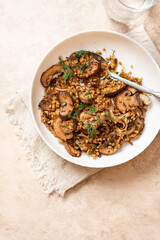 Spicy bulgur with mushrooms, onions, dill, and cumin in a bowl on a light background top view. Bulgur stewed with mushrooms. Arabic cuisine, vegan and vegetarian food. Copy space for text