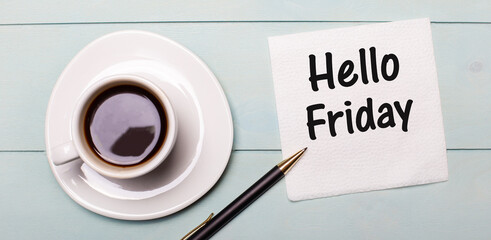 On a light blue wooden tray, there is a white cup of coffee, a handle and a napkin that says HELLO FRIDAY