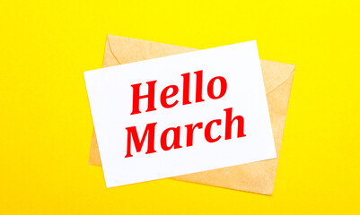 On a yellow background, an envelope and a card with the text HELLO MARCH. View from above