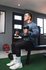 A fit athletic guy in a sweatshirt does seated dumbbell hammer curls. Working out and training...