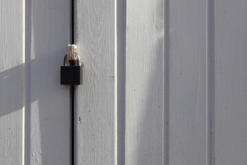 Black padlock on a white wooden door with sunlight and shadows. Minimalist concept image ideal for themes of security, privacy, protection, and simplicity