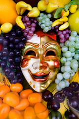 Smiling carnival mask surrounded by appetizing fruits. 
