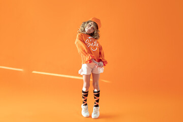 Photo of shy girl in full growth in fashionable clothes dance on orange background in cap and sweatshirt. Sunshine. Orange mhonchrome concept